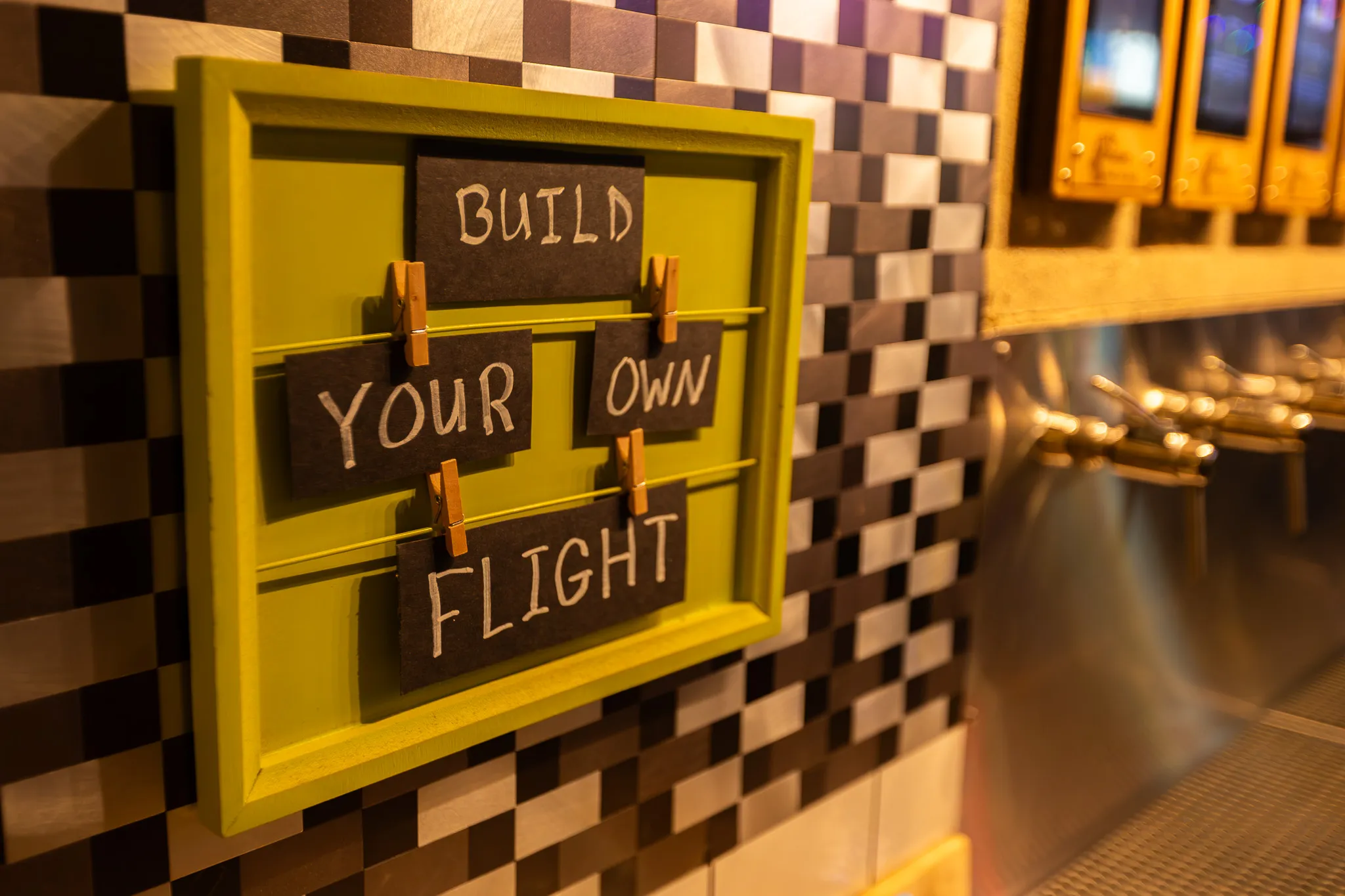 A hand-lettered "Build your own flight" sign hung on the checkered wood wall beside the taps