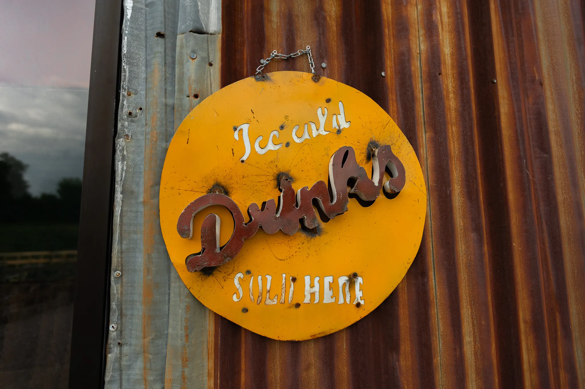 A vintage yellow enamel sign reading "Ice cold Drinks sold here" on rusted corrugated metal